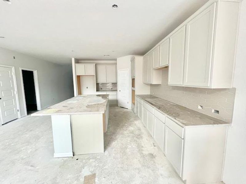 Kitchen featuring decorative backsplash, a center island, concrete floors, light stone counters, and white cabinetry Kitchen featuring decorative backsplash, a center island, concrete floors, light stone counters, and white cabinetry