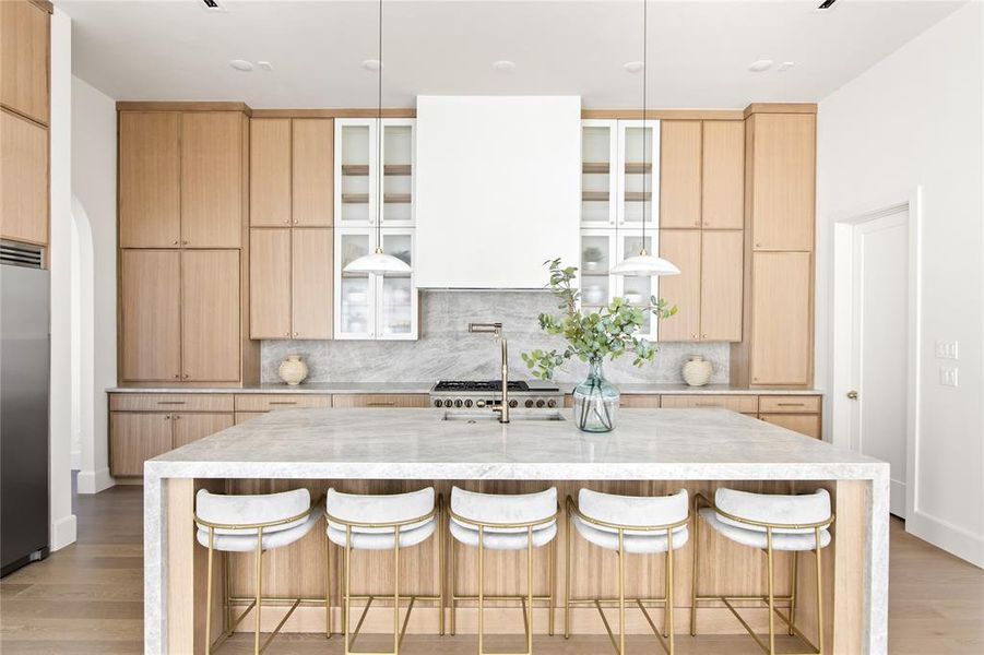 Gourmet kitchen featuring a waterfall-edge island with seating, natural wood-finish cabinetry, a large range with a custom hood, and marbled countertops with a matching backsplash