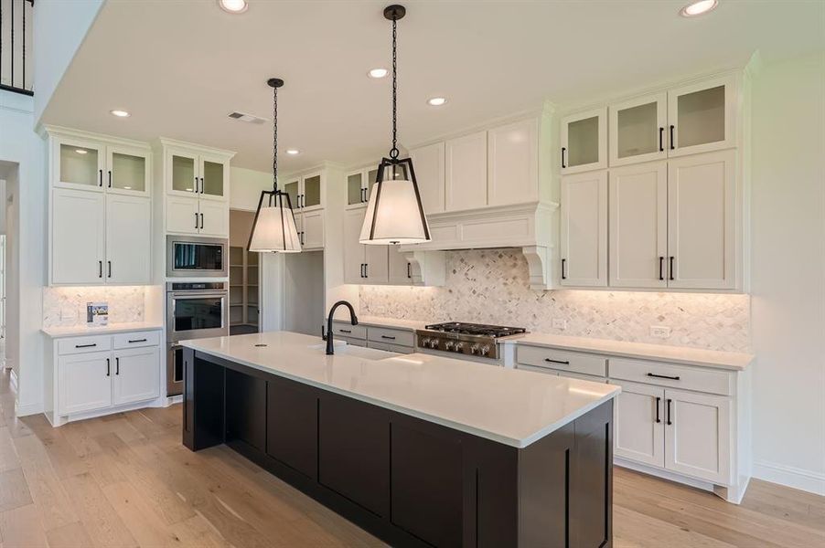 Kitchen with backsplash, appliances with stainless steel finishes, sink, and an island with sink