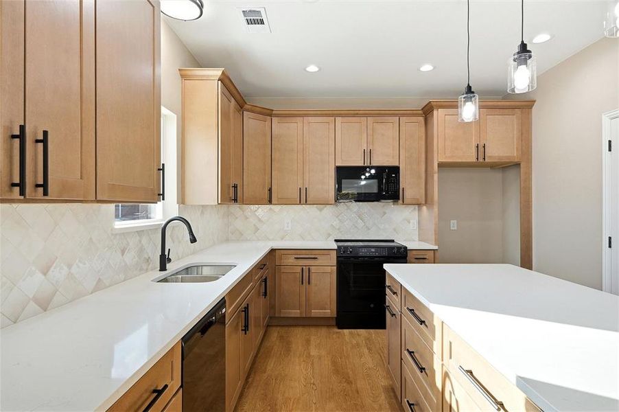 Kitchen featuring black appliances, pendant lighting, light wood-type flooring, light stone countertops, and backsplash Kitchen featuring black appliances, pendant lighting, light wood-type flooring, light stone countertops, and backsplash