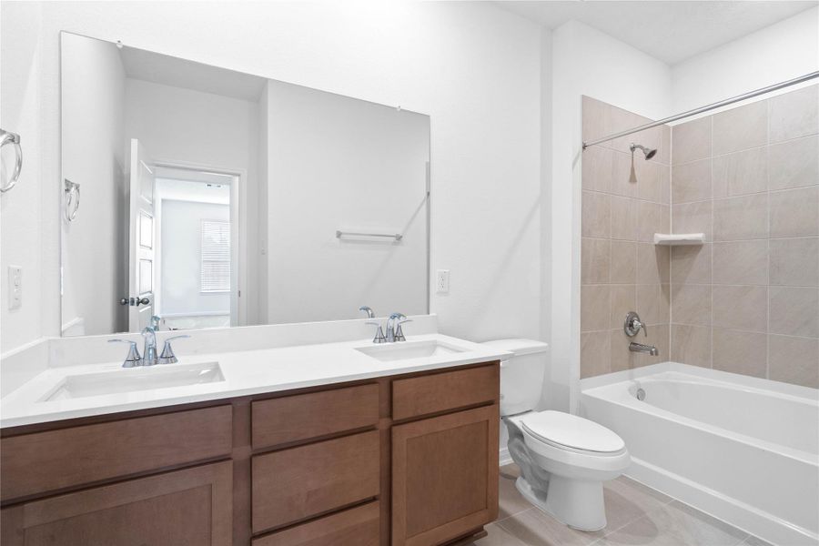This move-in ready primary bathroom offers a spacious tub/shower combination with a tiled surround, stained cabinetry topped with light countertops, dual sinks, high ceilings, neutral paint, a large mirror, and sleek, modern finishes for a polished look.