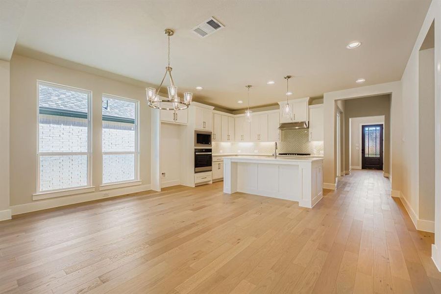 Kitchen with white cabinetry, light countertops, backsplash, a chandelier, and pendant lighting