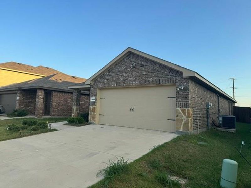 View of side of home with cooling unit, a garage, and a yard