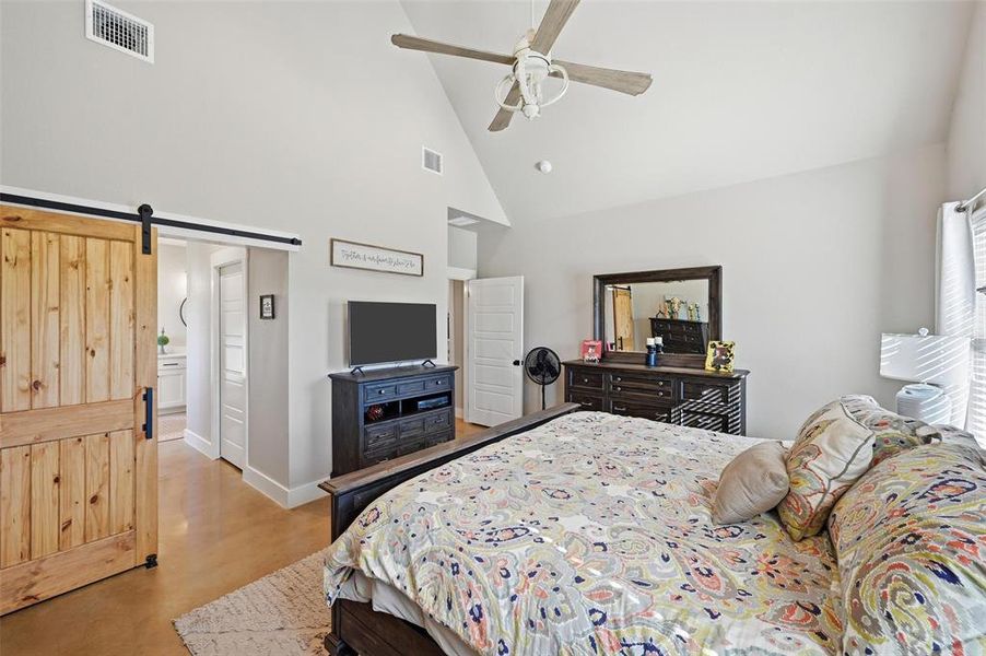 Bedroom with a barn door, high vaulted ceiling, ceiling fan, and ensuite bathroom Bedroom with a barn door, high vaulted ceiling, ceiling fan, and ensuite bathroom