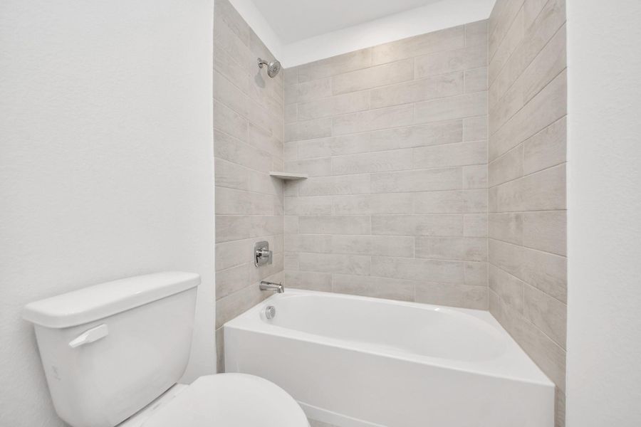 Secondary bath features tile flooring, bath/shower combo with tile surround, light stained wood cabinets, beautiful light countertop.