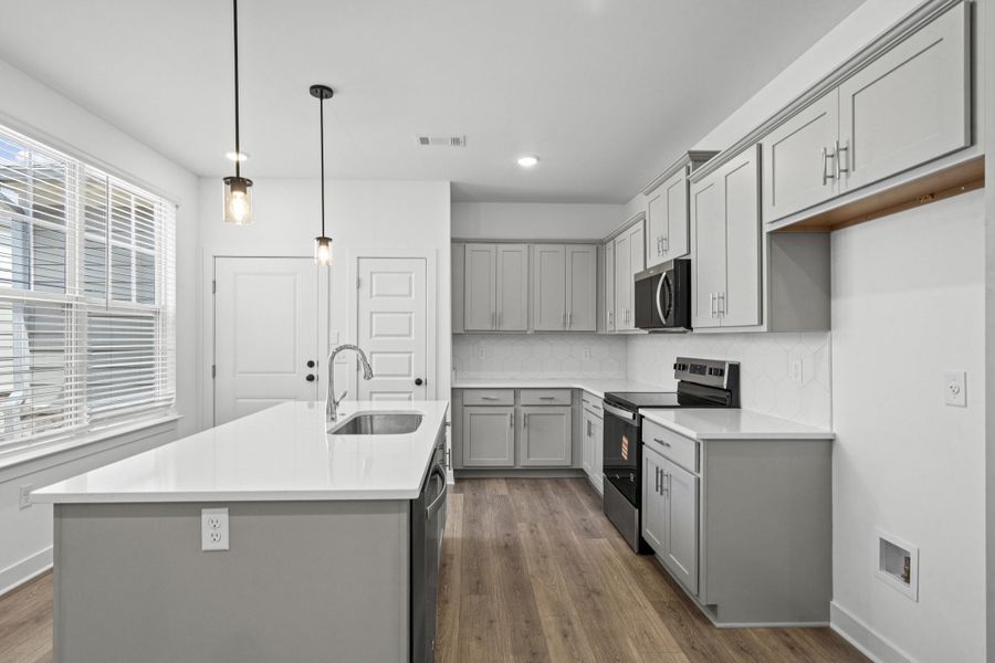 Modern kitchen featuring light gray cabinetry, stainless steel sink with a gooseneck faucet, white countertops, and wood-finish flooring