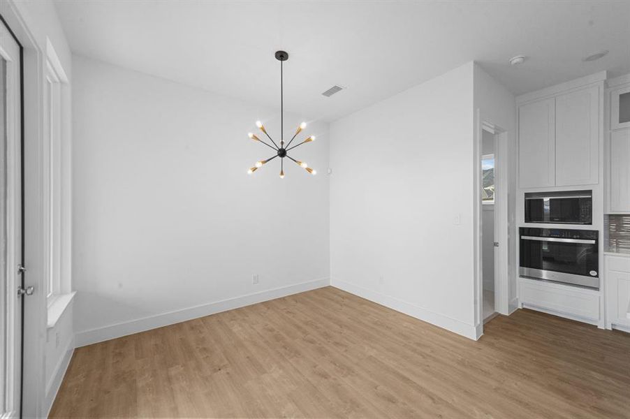 Unfurnished dining area with light wood finished floors, visible vents, baseboards, and an inviting chandelier