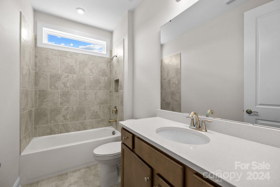 Secondary/Guest full Bath features tiled floors and walls with transom window and quartz counters.