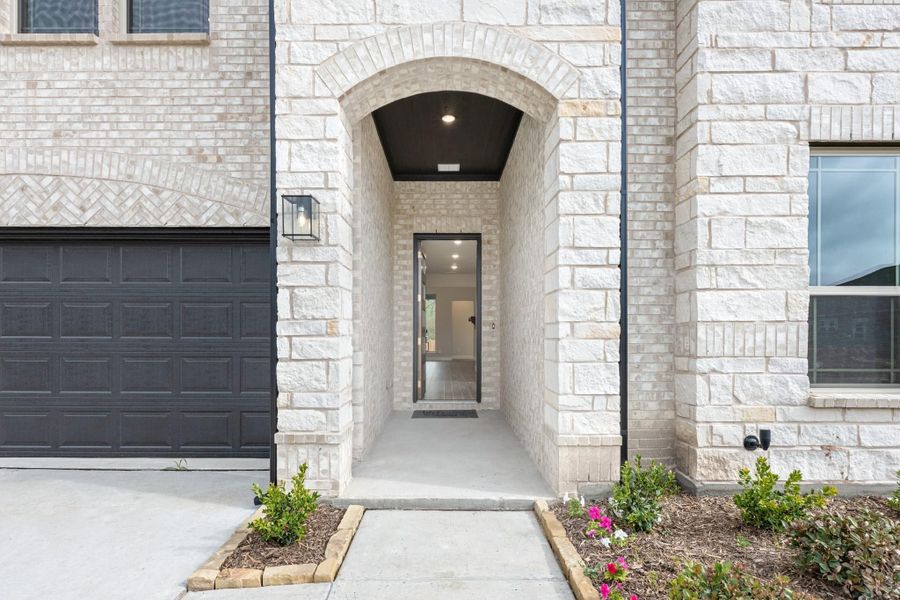 Home entrance with stone arch, dark front door, and garage next to landscaped walkway