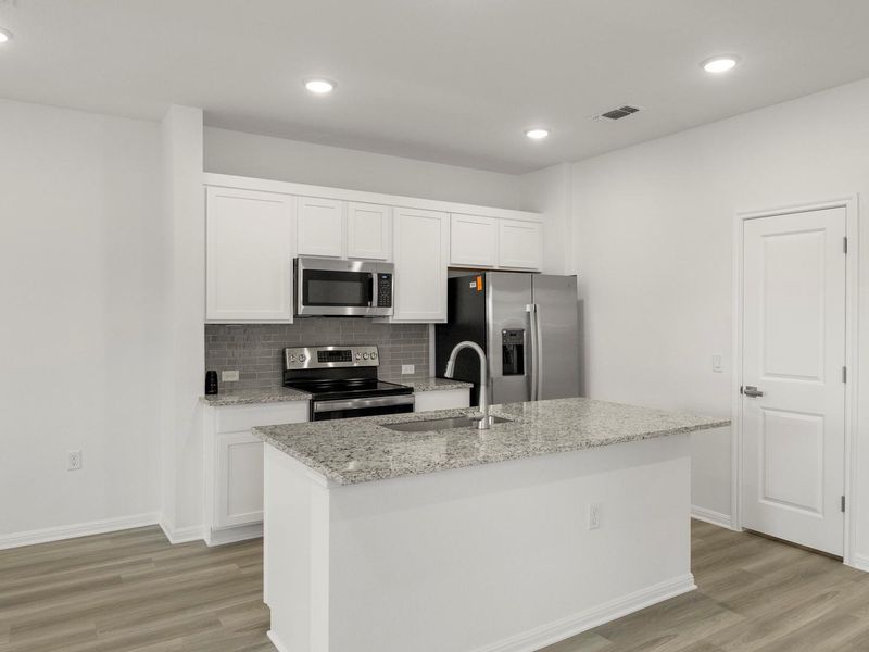 Modern kitchen with granite island and stainless steel appliances.