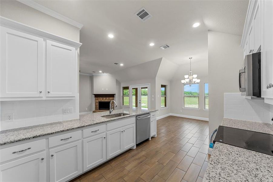 Kitchen featuring white cabinetry, light-toned granite countertops, a stainless steel sink with a gooseneck faucet, and wood-finish flooring