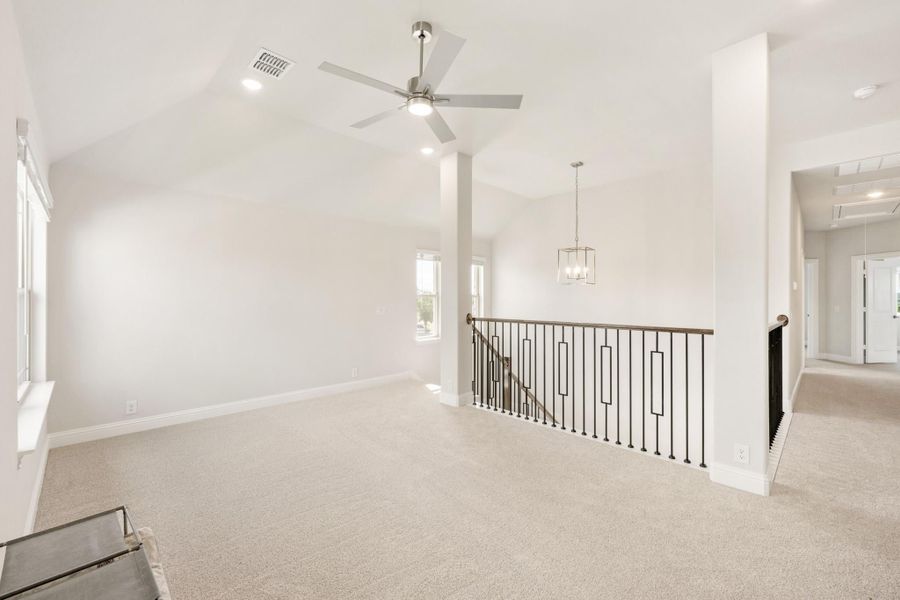 Open upstairs loft with vaulted ceiling, ceiling fan, iron stair railing, and neutral carpet