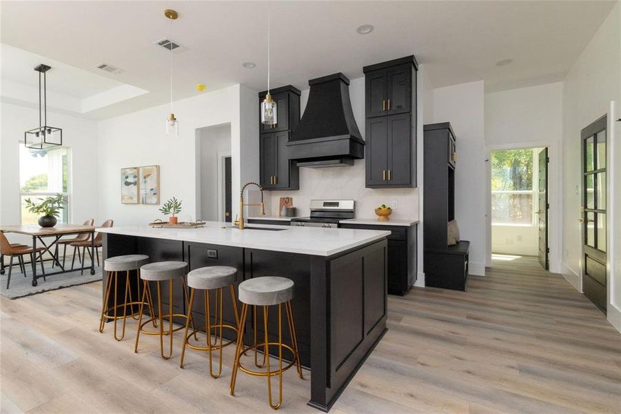 Kitchen with custom range hood, a kitchen island with sink, sink, decorative light fixtures, and stainless steel electric range