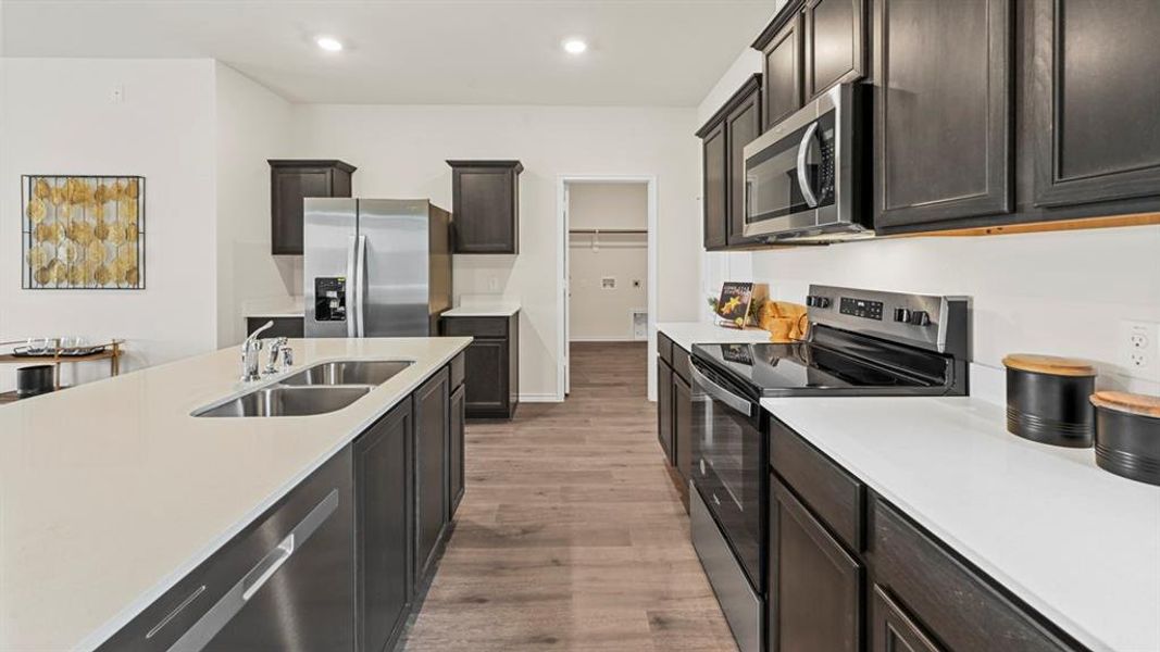Kitchen with stainless steel appliances, light wood-type flooring, light stone counters, recessed lighting, and dark wood finish cabinetry