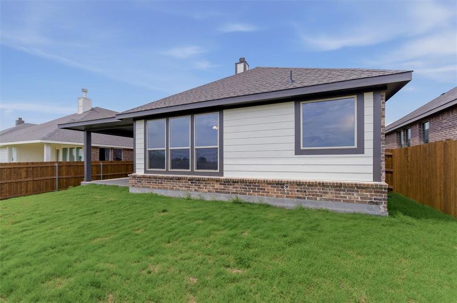 Expansive green lawn with a newly constructed exterior featuring white siding, a dark shingle roof, and a brick base Expansive green lawn with a newly constructed exterior featuring white siding, a dark shingle roof, and a brick base