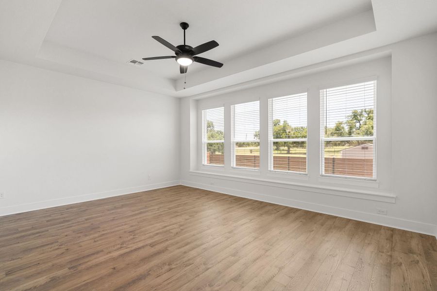 A tranquil primary bedroom with hardwood flooring and ample natural light from large windows.