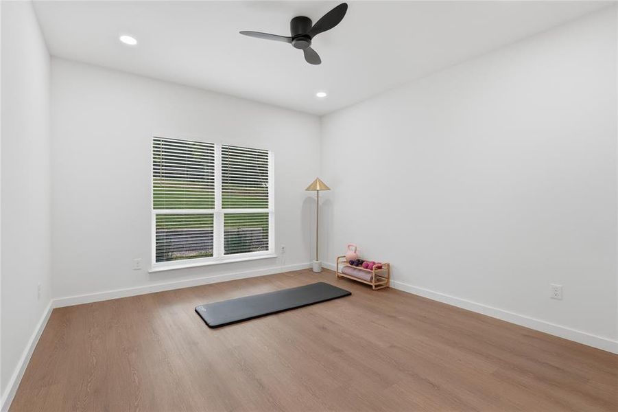 Spacious room featuring wood-finish flooring, white baseboards, and a modern ceiling fan