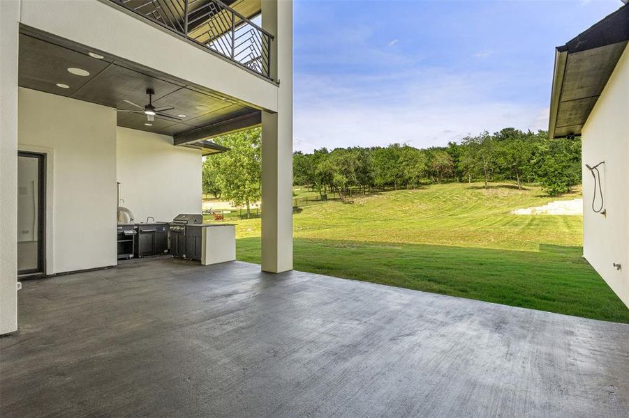 Covered outdoor living area with a built-in outdoor kitchen, concrete patio, and ceiling fan