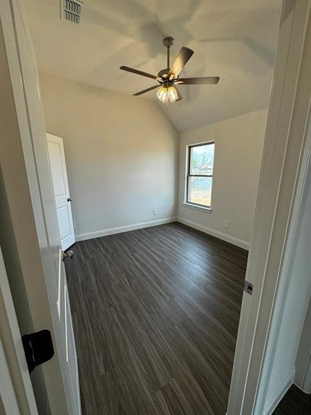 Spare room featuring dark hardwood / wood-style floors, vaulted ceiling, and ceiling fan