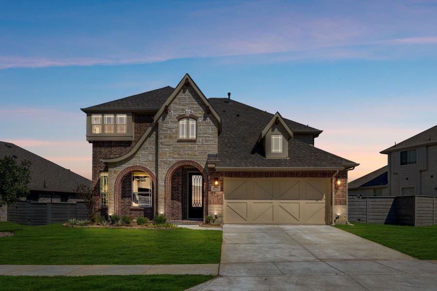 Two-story brick and stone home with arched entry, two-car garage, and concrete driveway at dusk