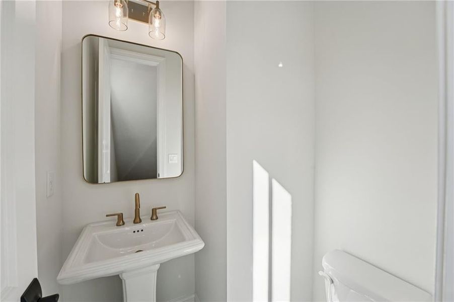 Powder bathrooms features pedestal style sink, framed mirrors and decorative light fixtures.  Image is of previously built Chamberlain Plan