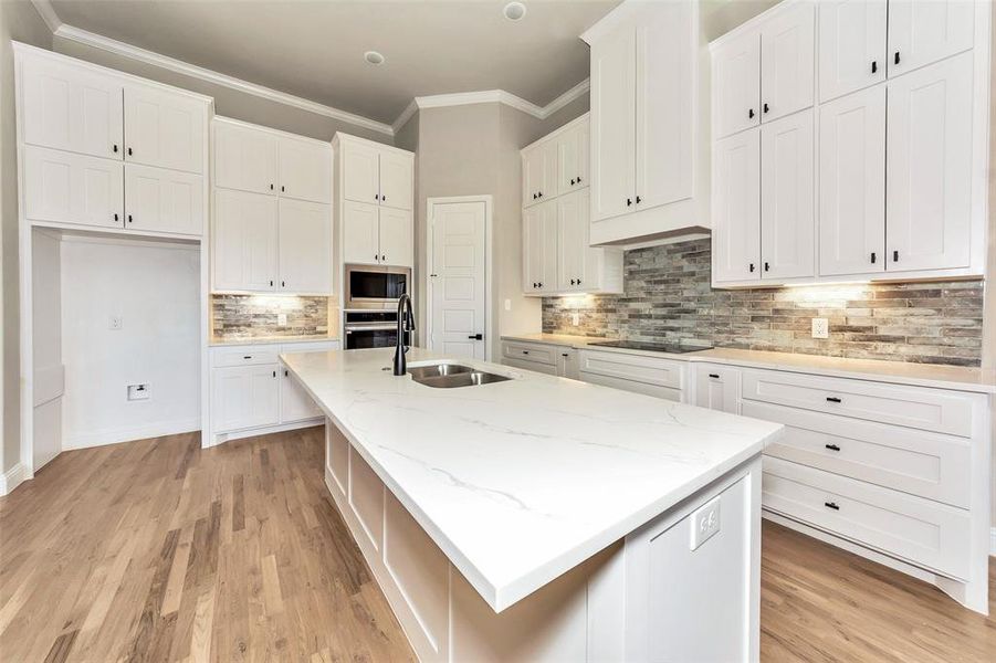 Kitchen featuring stainless steel appliances, decorative backsplash, light wood-type flooring, a kitchen island with sink, and white cabinetry