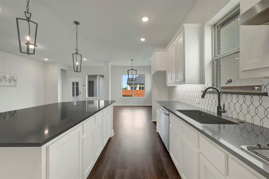 Kitchen featuring white cabinets, dark wood finished floors, pendant lighting, dishwasher, and dark stone counters