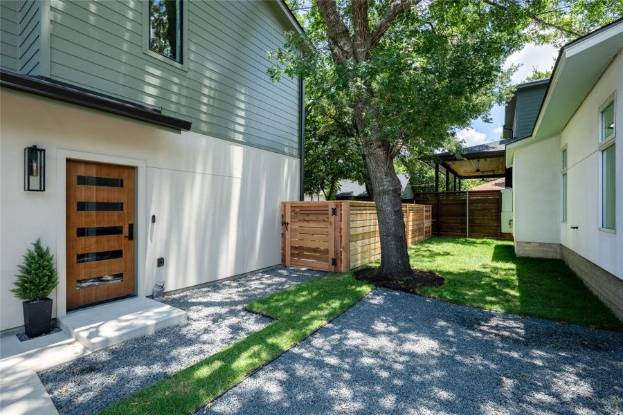 A modern entry door welcomes you to a private side yard with a well-maintained lawn and a discreet fenced enclosure. A modern entry door welcomes you to a private side yard with a well-maintained lawn and a discreet fenced enclosure.