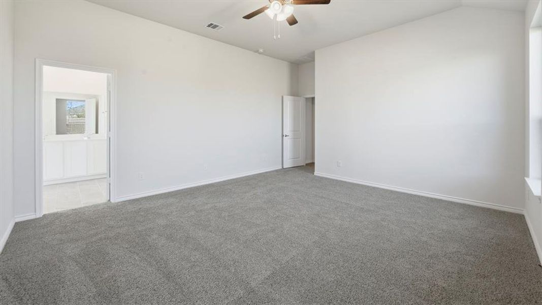 Spacious room featuring vaulted ceilings, neutral-toned carpet, a ceiling fan with integrated lighting, and a white paneled door