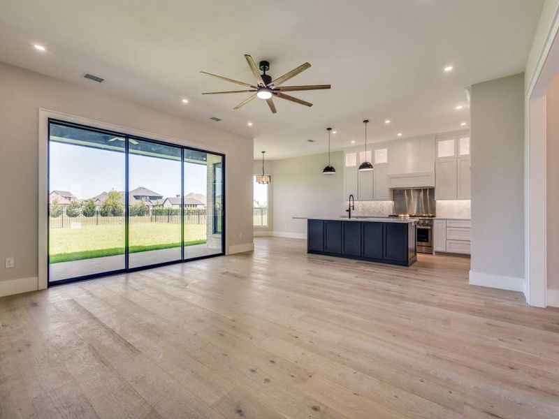 Living room with recessed lighting, baseboards, ceiling fan, light wood-type flooring, kitchen island, Custom Cabinets, Thor professional range-oven, Custom wood surround for ventilation over stove, Stainless backsplash for range,