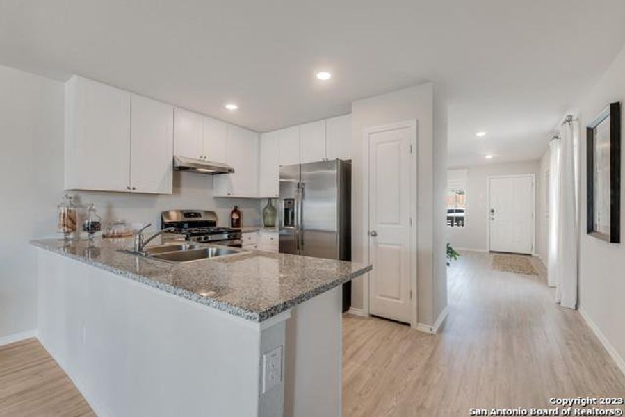 Kitchen featuring a peninsula, light wood-style flooring, light stone countertops, and recessed lighting Kitchen featuring a peninsula, light wood-style flooring, light stone countertops, and recessed lighting