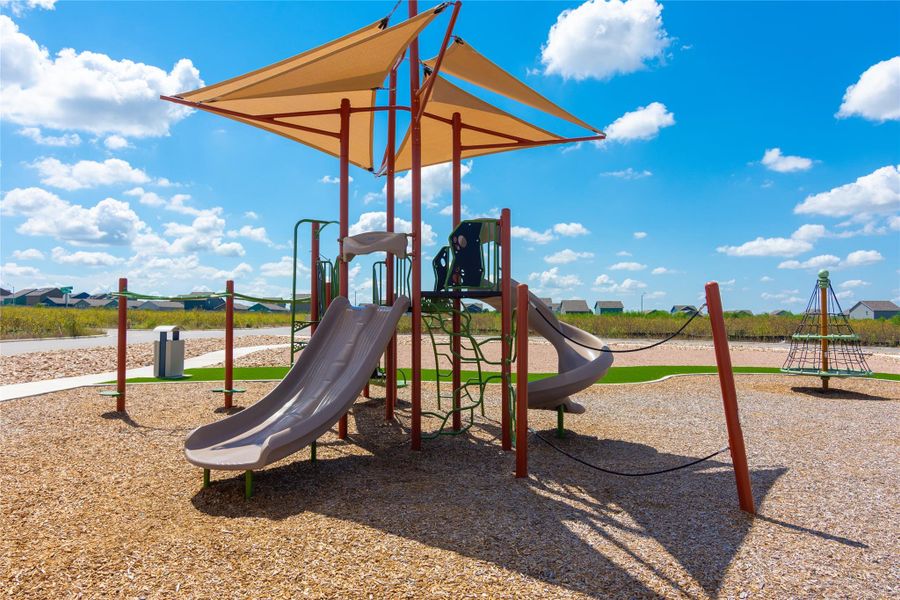 Community playground featuring shade canopies, multiple slides, a climbing structure, and a separate rotating play apparatus