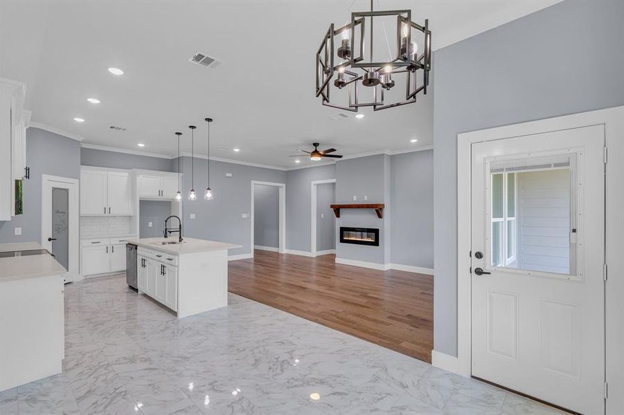 Kitchen with ceiling fan with notable chandelier, decorative light fixtures, a kitchen island with sink, and light tile floors