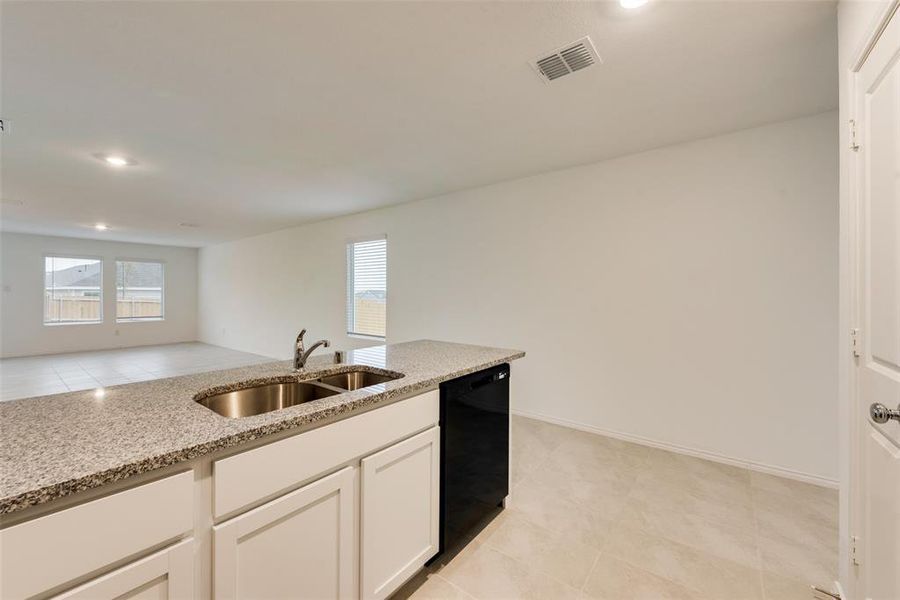 Kitchen with black dishwasher, sink, light stone counters, and white cabinetry