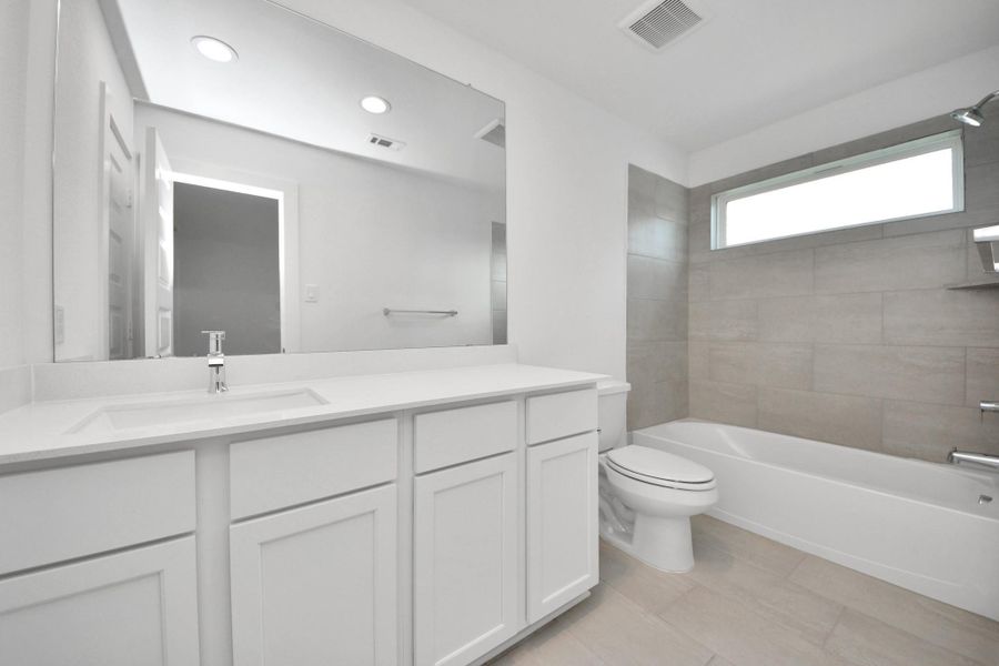 Secondary bath features tile flooring, bath/shower combo with tile surround, light stained wood cabinets, beautiful light countertop. Sample photo of completed home with similar floor plan. Actual colors and selections may vary.