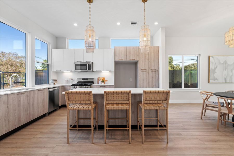 Sunlit kitchen featuring two-tone European-style cabinetry, quartz countertops & stainless steel appliances, designed with a large island perfect for dining & entertaining. Sunlit kitchen featuring two-tone European-style cabinetry, quartz countertops & stainless steel appliances, designed with a large island perfect for dining & entertaining.