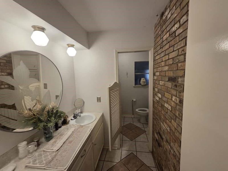 Bathroom with light tile patterned floors, brick wall, and double vanity Bathroom with light tile patterned floors, brick wall, and double vanity