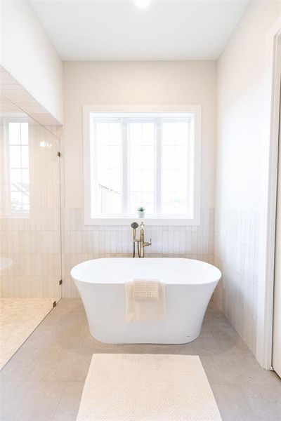 Freestanding soaking tub with a floor-mounted brass faucet, set against a backdrop of vertical tile wainscoting