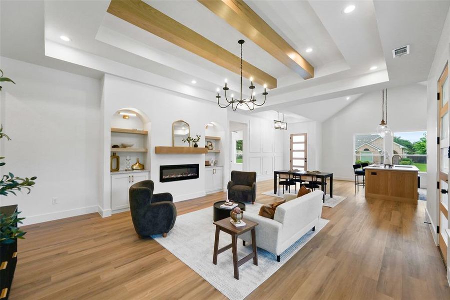 Spacious living area featuring wood-finish flooring, a contemporary electric fireplace with a wood mantel, built-in shelving, and a vaulted ceiling with exposed wood beams and recessed lighting