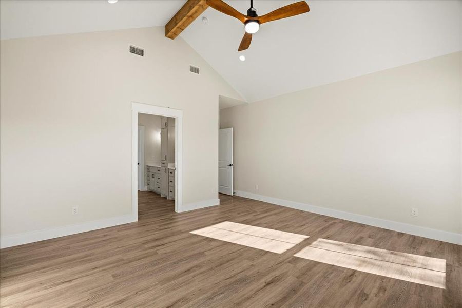 Bedroom with beamed ceiling, light wood-style floors, high vaulted ceiling, ceiling fan, and ensuite bath