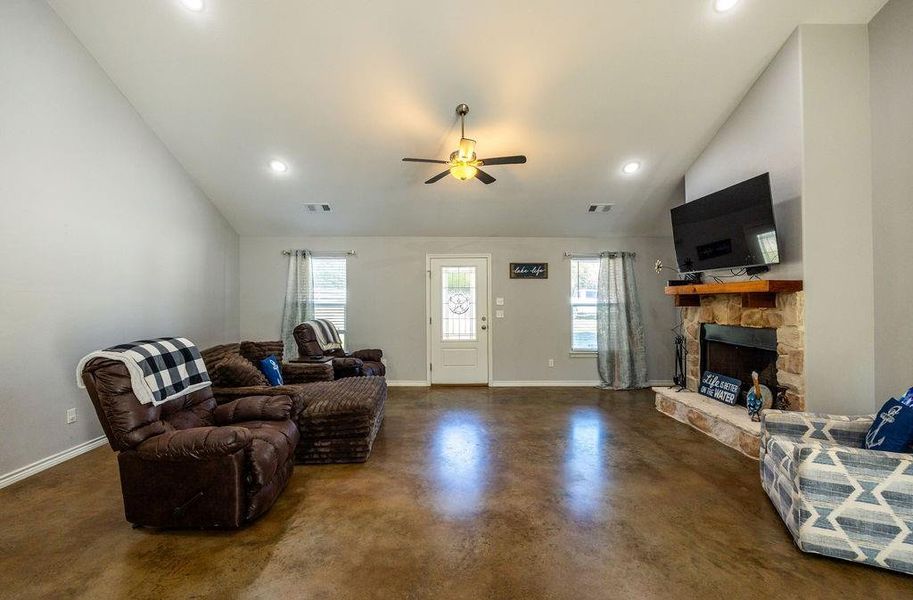 Living area featuring lofted ceiling, a fireplace, concrete floors, recessed lighting, and a ceiling fan