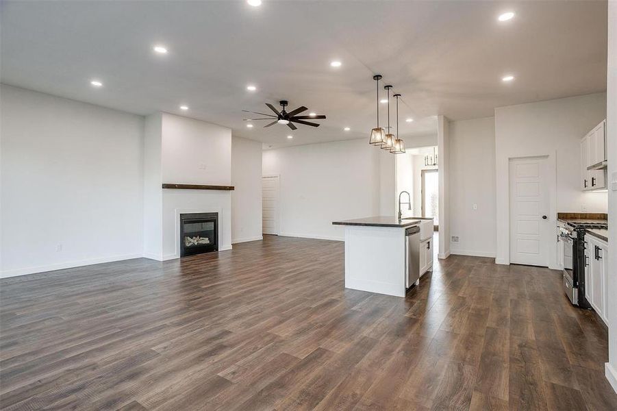 Kitchen with decorative light fixtures, white cabinets, ceiling fan, a kitchen island with sink, and appliances with stainless steel finishes