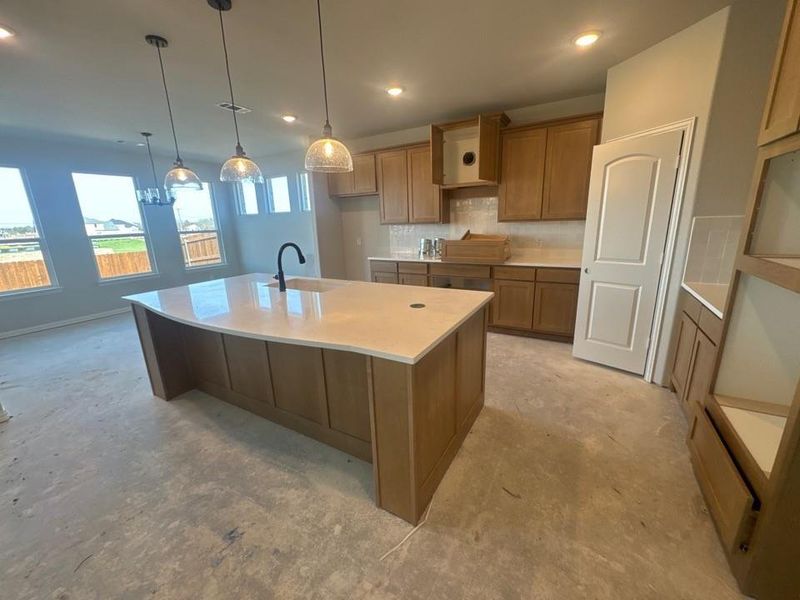 Kitchen with wood finish cabinetry, a large island, unfinished concrete floors, backsplash, and light stone countertops