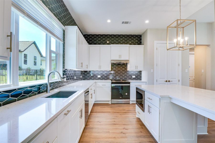 Kitchen with sink, stainless steel appliances, white cabinetry, and decorative light fixtures