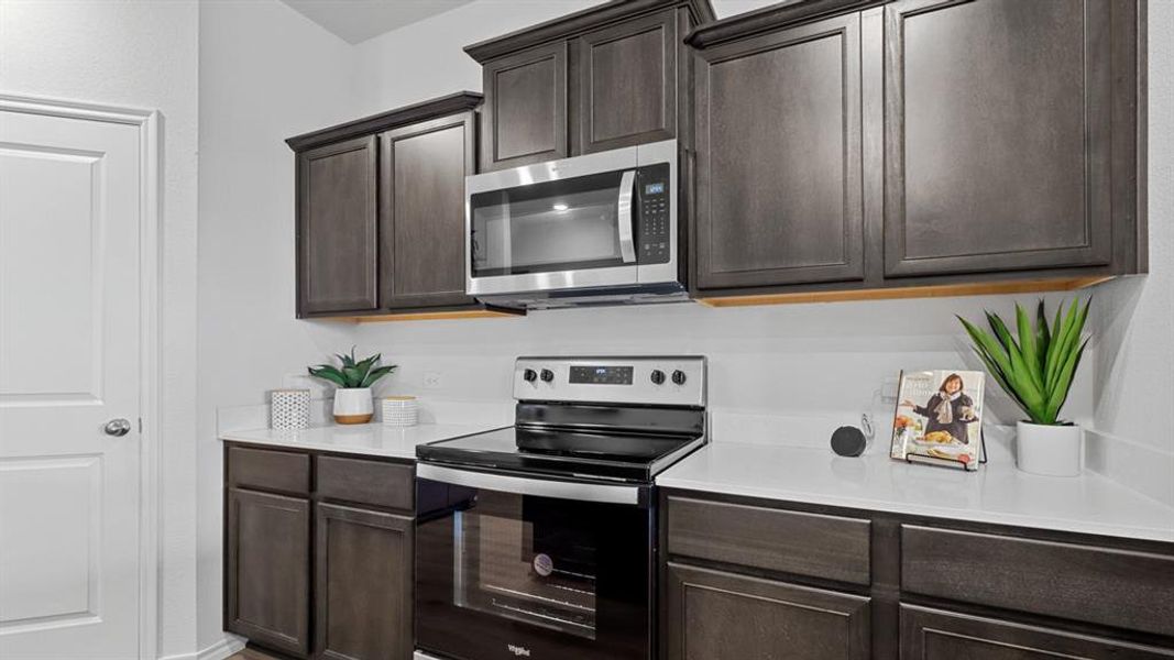 Kitchen featuring stainless steel appliances, dark wood finish cabinetry, and light stone countertops Kitchen featuring stainless steel appliances, dark wood finish cabinetry, and light stone countertops