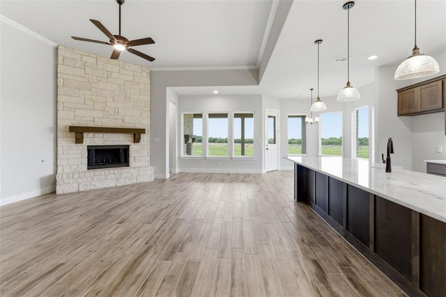 Living space with wood-finish flooring, a stone-clad fireplace featuring a dark wood mantel, and a ceiling fan with integrated lighting