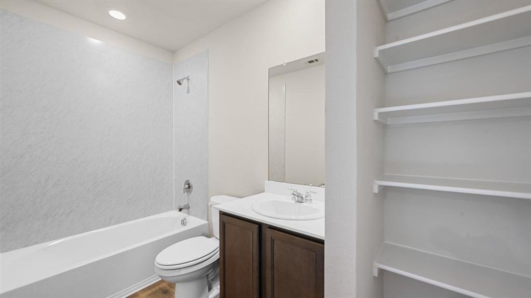 Bathroom featuring a white bathtub with integrated shower, single vanity with dark wood-finish cabinetry, and built-in shelving