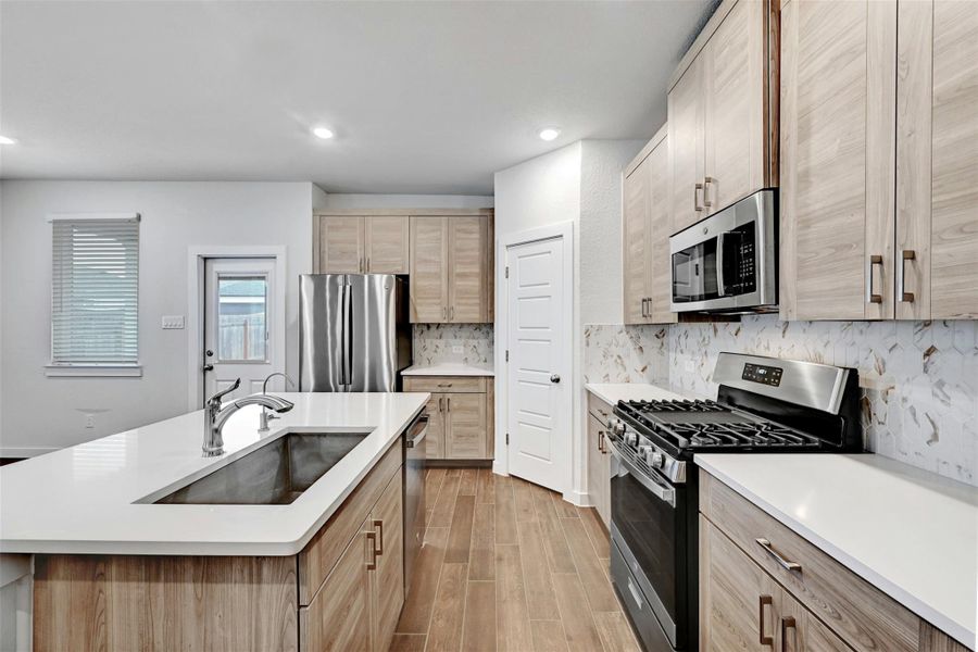 Kitchen featuring stainless steel appliances, light brown cabinetry, light countertops, backsplash, and recessed lighting Kitchen featuring stainless steel appliances, light brown cabinetry, light countertops, backsplash, and recessed lighting