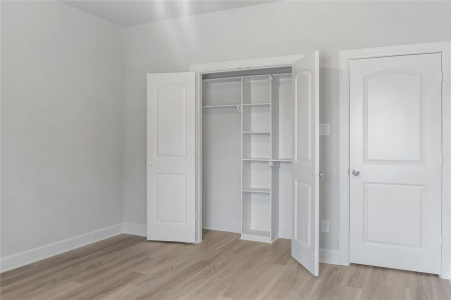 This photo shows a bright, minimalistic room with light-colored walls and wood flooring. It features a closet with open double doors and built-in shelving, and an additional closed door, offering ample storage space.
