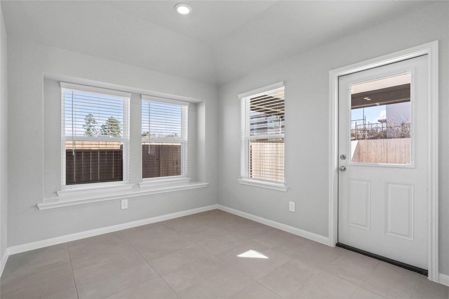 Enjoy meals in this sun-drenched space, featuring durable tile flooring, abundant natural light from the large windows (fitted with blinds), window seat, high ceiling, and recessed lighting. An access door is conveniently placed for access to the rear covered patio and backyard.